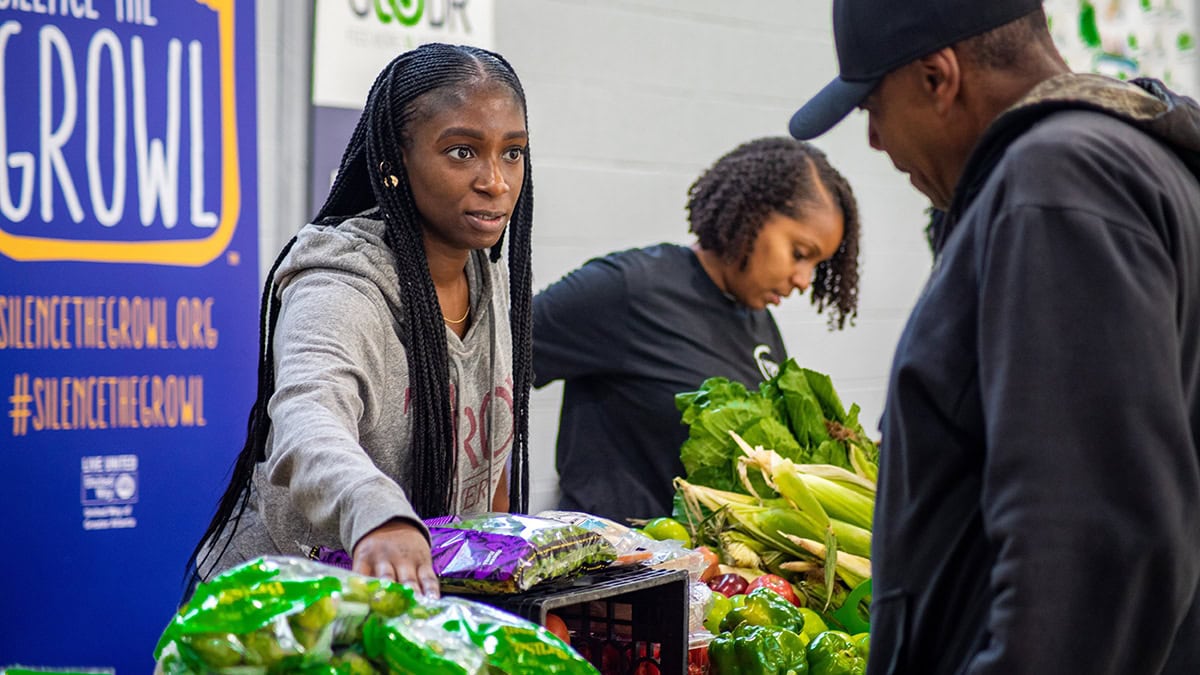 Woman volunteer giving out fresh produce to a man at a free food distribution site in Atlanta